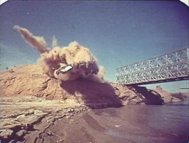 The still from the 'Double Bill: 'Dirty Mary, Crazy Larry' and 'Vanishing Point'' TV spot trailer depicts a dramatic scene of a car launching off a sandy incline, creating a cloud of dust and debris as it approaches a bridge. This image likely emphasizes the high-octane action and excitement characteristic of both films. The vibrant colors and dynamic composition suggest a vintage aesthetic, typical of reissue trailers from that era.