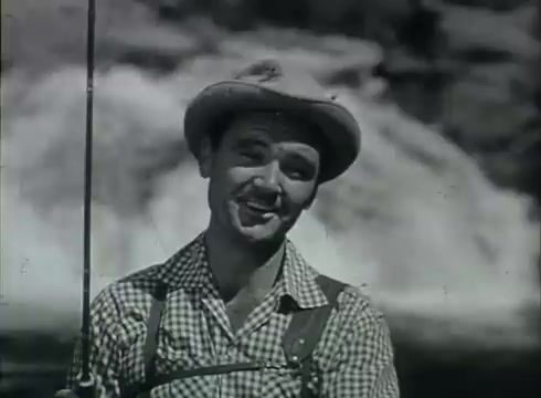 The still captures a cheerful man in a fishing setting, wearing a checkered shirt and a broad-brimmed hat. He holds a fishing rod and appears to be speaking directly to the audience, likely promoting the Gillette Slim Adjustable razor. In the backdrop, a waterfall hints at a rugged outdoor theme, characteristic of 1960s advertising that associates masculinity with nature and leisure. The overall tone reflects a blend of charm and practicality, typical of the era's commercials.   Follow us on Twitter @FromFilm.