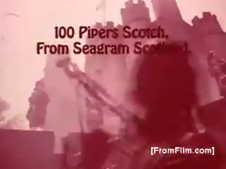 The still features a vintage advertisement for Seagram's 100 Pipers Scotch from the 1970s, set against a backdrop that suggests Scottish heritage. The text prominently displays the brand name, highlighting its origins. The image likely evokes a celebration or cultural event, typical of the era's advertising style. The colors and quality reflect the 16mm film format.