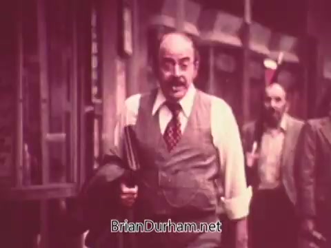 The still from 'Ohio Job Service PSA 3 - 1970s' shows a man in a suit, walking with purpose. He has a mustache and is carrying a jacket, appearing confident. The background features other individuals, suggesting a busy urban setting. The color tone is warm, typical of vintage film from that era. The overall vibe reflects a professional atmosphere, likely related to job seeking or employment.