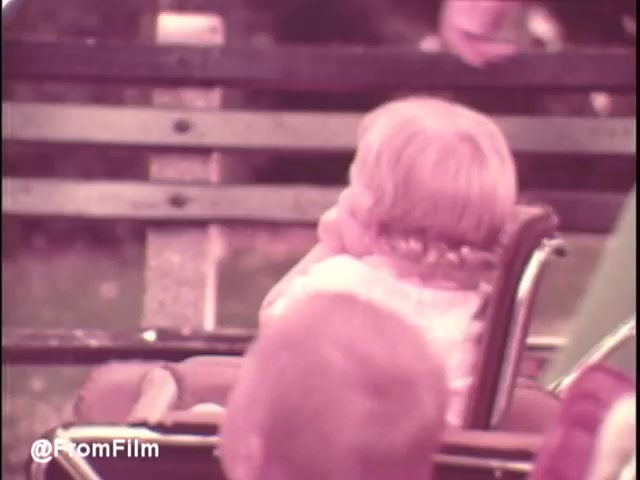 The still from the 'Pamper's Diapers' commercial features a young child with light-colored hair, sitting in a stroller and gazing off to the side. The background includes blurred park elements, suggesting a casual outdoor setting. The color tone of the image is warm, characteristic of early 1970s film processing. The overall mood appears cheerful and child-friendly, fitting for a diaper advertisement aimed at parents. Follow us on Twitter @FromFilm for more nostalgia!