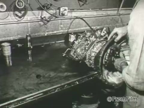 The still from the 1968 PSA by the American Foundation for the Blind shows a person working on a mechanical engine or machinery in a workshop setting. The environment appears industrial, with tools and parts scattered around. This imagery likely symbolizes the themes of empowerment and capability for individuals with vision loss, emphasizing the importance of fostering independence and accessibility in various fields, including technology and mechanics.