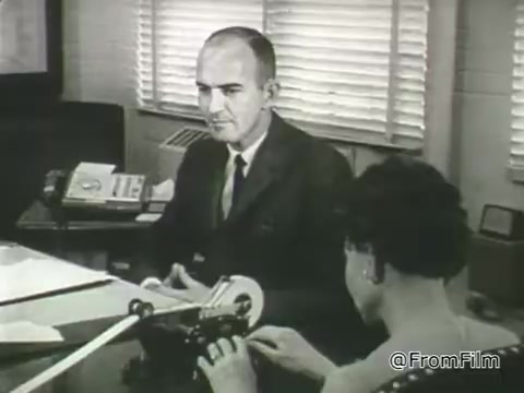 The still from the 1968 PSA by the American Foundation for the Blind features a man and a woman in an office setting. The man, dressed in a suit, appears to be engaged in conversation while seated. The woman, using a machine that facilitates communication or note-taking, concentrates on her task. The background includes office equipment, suggesting a professional environment focused on accessibility and support for individuals with vision loss. The visual emphasizes the theme of empowerment and independence for people with disabilities.