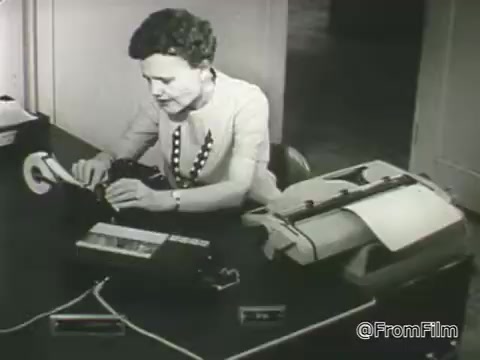 The still from the 1968 PSA for the American Foundation for the Blind features a woman seated at a desk, using a typewriter and a device likely related to assistive technology for individuals with vision loss. She is intently focused on her task, illustrating the organization's commitment to improving accessibility and independence for people with vision impairments. The setting appears professional, emphasizing the importance of resources and tools in promoting quality support and information for those affected by vision loss.