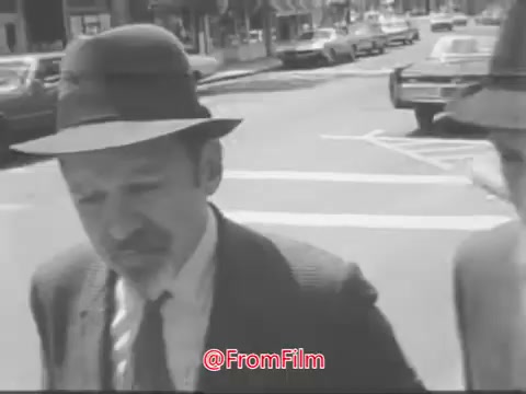 The still from the 'Guideposts Magazine PSA - 1968' features two men walking on a street, dressed in formal attire and hats. One man appears to be deep in thought, possibly reflecting on the conversation as they navigate the urban environment. The scene captures a moment of dialogue, likely related to appreciating the simple joys of life and nature. The black-and-white aesthetic adds a classic, nostalgic feel to the image.