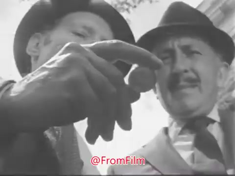 The still features two men in hats, closely examining a small object held in one man's hand. The focus on the object suggests curiosity or discovery. The scene conveys a sense of intrigue, aligning with the voice-over's theme of appreciating the wonders of nature and small moments in life.