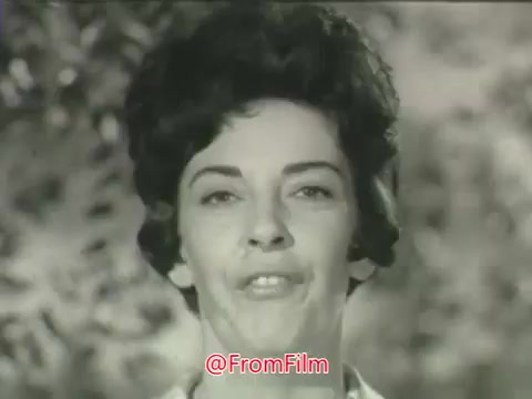The still from the 'Cold Power detergent commercial' features a close-up of a woman speaking directly to the camera. She has a confident demeanor with neatly styled hair typical of the 1960s. The background is blurred, focusing attention on her expression as she discusses her thoughts on laundry concerns, specifically clothing shrinkage. The commercial aims to convey reassurance regarding the effectiveness of Cold Power detergent, presenting relatable testimonials from everyday women.