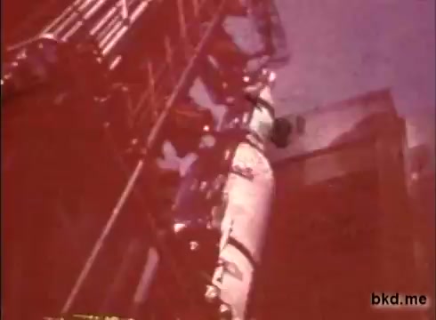 The still from 'Apollo 12 pre-launch unknown film' showcases a scene likely set at the launch pad, featuring a Saturn V rocket. The rocket is being prepared for its impending launch, surrounded by support structures and equipment. The film appears to capture the meticulous process of pre-launch preparations, emphasizing the technical details involved. The coloration suggests the vintage nature of the 16mm print, adding a nostalgic aesthetic to the imagery. Overall, it reflects the excitement and energy surrounding the Apollo 12 mission.