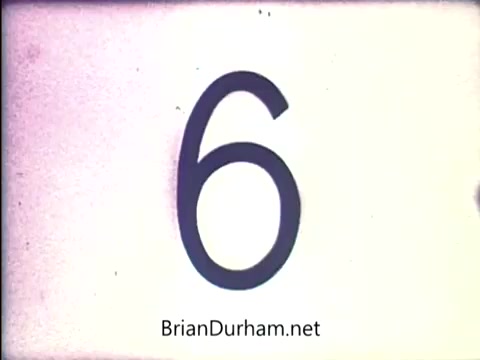 The still features a large, bold number '6' displayed prominently against a light background. This frame is from a 16mm film related to the 'Lazy Dazy' doll by Ideal, dating back to the early 1970s. The image has a vintage quality typical of that era's home movies or promotional footage.