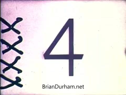 The 16mm still features a large, bold numeral '4' prominently displayed on a light background. To the left, decorative elements, possibly stitching or embroidery lines, create a visual contrast. The imagery has a vintage aesthetic typical of early 1970s media, likely related to a promotional or instructional context for the 'Lazy Dazy' doll from Ideal.