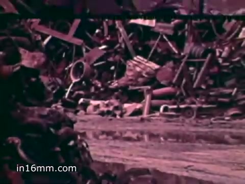 The still from 'Pat Paulsen PSA for the Environment Protection Agency - 1970's' depicts a cluttered junkyard filled with various discarded items. Piles of metal, appliances, and debris create a stark visual representation of waste. The voiceover highlights alarming statistics about solid waste production in the U.S., emphasizing the extensive amounts of cans, bottles, plastics, and other materials being thrown away annually. The imagery serves to illustrate the urgent need for environmental awareness and waste management.