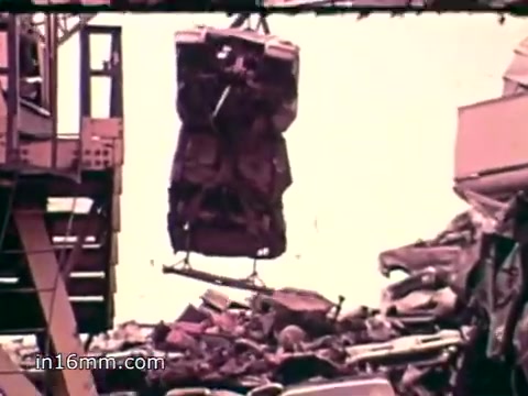 The still depicts a junkyard scene where a crane lifts a crushed car from a pile of refuse. The background shows a chaotic landscape of discarded items, emphasizing the overwhelming amount of solid waste generated annually in the U.S. The visual underscores the urgency of environmental issues presented in the voiceover, which details the staggering statistics of waste production and disposal.