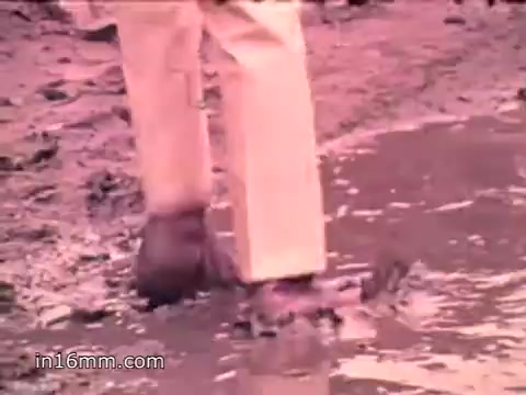 The still from the PSA features a person standing in muddy water, likely reflecting environmental pollution. The focus on their feet emphasizes the messy, hazardous conditions caused by waste, underscoring the message regarding the significant solid waste problem in the U.S., as highlighted in the voiceover. The scene likely aims to evoke concern and raise awareness about environmental protection.