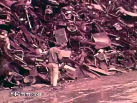 The still from the 1970s PSA featuring Pat Paulsen shows a person standing in front of a large, chaotic pile of scrap metal and discarded materials. This visual highlights the overwhelming issue of solid waste in the United States, which the voiceover stresses is in the millions of tons annually. The imagery serves to convey the environmental impact of excessive waste production, reinforcing the urgency of addressing pollution and promoting sustainability.