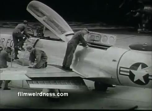 The still depicts a scene from a 1950s-1960s U.S. Air Force Public Service Announcement. It shows several personnel working on an aircraft, with one individual accessing the cockpit area. The aircraft features the U.S. Air Force insignia. The atmosphere suggests a focus on maintenance and preparation, highlighting the technical aspects of military aviation.