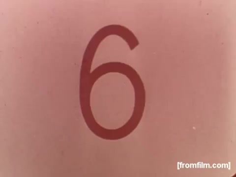 The still features a large, bold numeral '6' against a soft pink background. The number is stylized, with a prominent outline that gives it a three-dimensional effect. This still likely serves as part of a countdown or indicator related to the Colgate Dynamo Liquid Detergent commercial from the 1970s. The overall aesthetic reflects the design trends of that era in advertising, emphasizing simplicity and clarity.