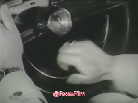 The still features a close-up of a driver's hands gripping the steering wheel of a car. The focus emphasizes the action of turning or adjusting the wheel, highlighting the context of driving. This imagery is part of a 1960s Aetna public safety message aimed at raising awareness about the dangers of speeding and reckless driving. The black-and-white aesthetic reflects the era's style and adds to the urgency of the safety message.