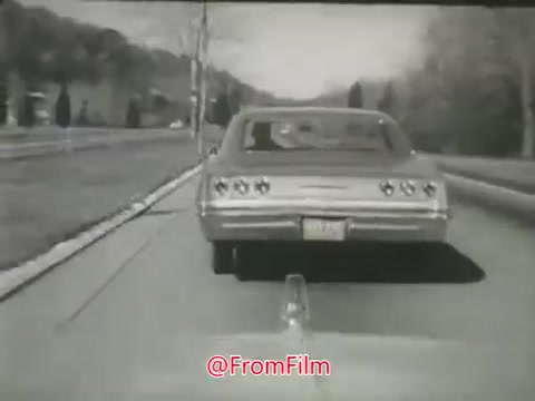 The still features a classic car driving down a two-lane road in a rural setting, characteristic of the 1960s. The scene emphasizes the straightforwardness of the road, which is framed by trees and vegetation on both sides. The film likely conveys a message about the risks associated with speeding and dangerous driving, typical of public safety campaigns from that era. The visual tone is likely black and white, reflecting the film’s time period and purpose.