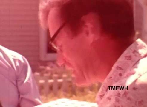 The still from 'Birdseye New England Style Vegetables' features a man with glasses and a patterned shirt, engaged in a moment that appears to involve conversation or interaction with another person partially visible. The color tone is warm, suggesting a sunny outdoor setting, likely conveying a friendly and casual atmosphere. The background hints at a suburban environment with a fence and a house.