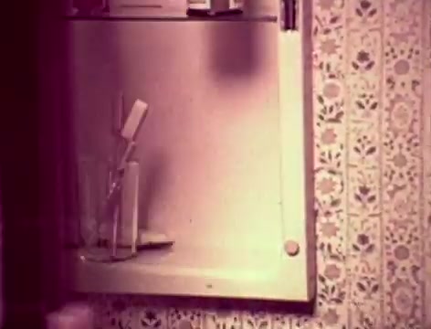 The still from the 1970s Listerine commercial showcases a bathroom setting. There’s a mirrored medicine cabinet with a toothbrush and a glass, typical for personal hygiene. The vintage wallpaper adds to the nostalgic feel. The conversation highlights a father’s concern about communication with his son and bad breath, introducing Listerine as a solution. The tone reflects familial interaction and addresses common concerns about oral health.