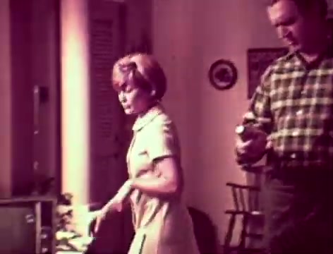 The still from the 'Listerine Commercial - 1970s' depicts a domestic scene with a mother and father. The father appears concerned about his relationship with their son, questioning if he has 'bad breath.' The mother suggests using Listerine, explaining its benefits for fresh breath. The father shows hesitation, implying that he finds Listerine too strong. The setting likely reflects a typical family home of that era, emphasizing everyday concerns about communication and personal hygiene.