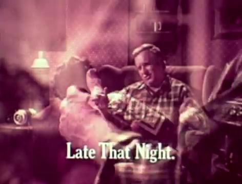 The still from the 1970s Listerine commercial depicts a father sitting in a cozy living room, wearing a plaid shirt. He appears concerned while holding a large bottle of Listerine, reflecting on his son's silence and his own perceived shortcomings. The text 'Late That Night' suggests a transition to an evening scenario, implying that the father will take action later to address his bad breath concerns. The overall tone conveys humor mixed with a relatable family dynamic.