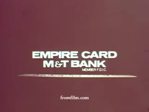 The 16mm still features bold, white text on a simple maroon background, reading 'EMPIRE CARD M&T BANK MEMBER FDIC.' The design is minimalistic, characteristic of 1970s advertising, emphasizing the bank's branding and reliability.