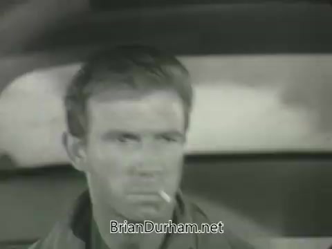 The still features a serious-looking man with a cigarette in his mouth, sitting in a car. His expression suggests tension or contemplation, and the surroundings appear blurred, emphasizing his focus. The black-and-white imagery reflects the era of the 1963 promotions.