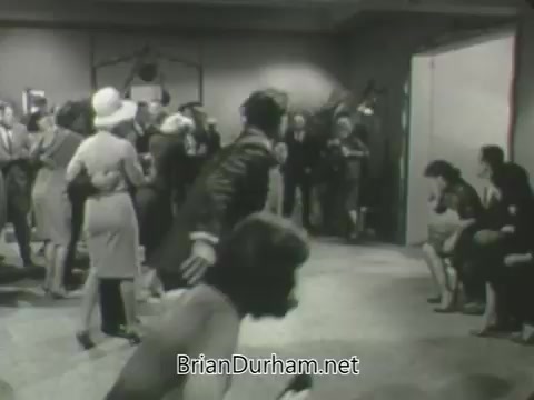 The still from the 'ABC Fall 1963 season promos' showcases a lively indoor scene, likely depicting a social gathering. It features a mix of elegantly dressed individuals, some engaged in conversation, while others sit and observe. The atmosphere suggests a vibrant, dynamic setting typical of early 1960s entertainment promos, emphasizing style and social interaction.