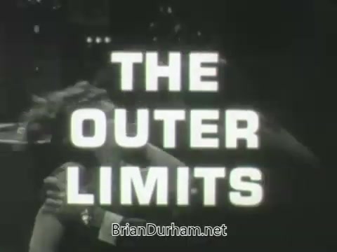 The still features the bold title 'THE OUTER LIMITS' prominently displayed in large, white text. The background appears to depict a scene from the show, likely featuring dramatic or intense action, with a focus on characters interacting closely. The overall aesthetic aligns with mid-20th century television promotional materials, capturing the show's sci-fi essence.