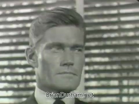 The still features a close-up of a man with a serious expression, wearing a suit and tie. The background consists of horizontal blinds, creating a stark, dramatic lighting effect. The shot conveys a sense of intensity or contemplation, typical of promotional material from the 1960s.