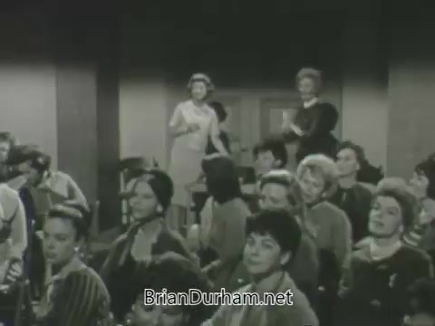 The still from the 'ABC Fall 1963 season promos' features a group of women in a studio audience, with several standing and engaging. The setting appears to be a television studio, characterized by a classic 1960s aesthetic. The women show varied expressions, from excitement to attentiveness, indicating their involvement in the promotional event. The overall atmosphere is lively and engaging, typical of television promotions from that era.