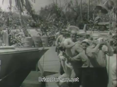 The still from 'ABC Fall 1963 season promos' features a group of people gathered around a boat at a dock, likely in a tropical setting with palm trees in the background. The mood appears lively, as the individuals seem engaged and cheerful, possibly celebrating or welcoming someone. The scene captures a vintage ambiance reflective of 1960s television promotional content.