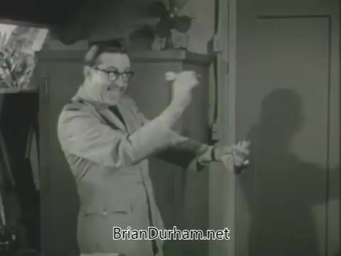 The still features a man in a light-colored jacket and glasses, animatedly gesturing with a smile. He appears to be interacting with a door, possibly capturing a comedic moment. The setting is informal, hinting at a playful tone typical of promotional content from the 1963 ABC fall season. Shadows and lighting suggest a studio environment.