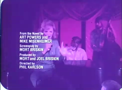 The still from the 'Framed' trailer features a woman performing on stage, likely at a club, with a band in the background. The image has a vintage look, consistent with 16mm film quality, and displays credits for the creators, including writers and producers. The overall color palette appears purple, enhancing the nostalgic feel.