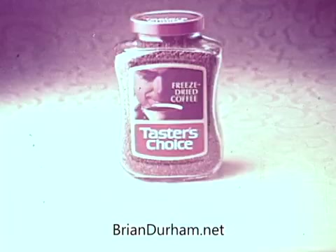 The still features a jar of Taster's Choice freeze-dried coffee, prominently displaying its brand name. The background has a subtle texture, enhancing the focus on the coffee jar, typical of vintage advertisements. The commercial likely emphasizes the product's quality and appeal, consistent with the era's marketing style.