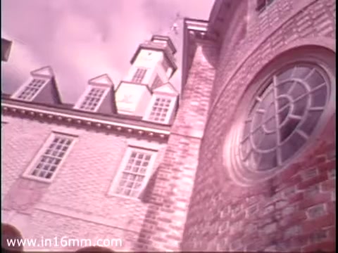 The still from the 'Bicentennial Youth Debates' PSA depicts a historic building with distinctive architectural features, such as a clock tower and large windows. The brickwork is prominent, suggesting a classic, colonial-style structure. The lighting appears soft, contributing to a nostalgic ambiance. This visual aligns with the context of the Bicentennial Youth Debates, emphasizing themes of American heritage and civic engagement. The program, supported by the Speech Communication Association and the National Endowment for the Humanities, aimed to engage youth in discussions about important societal issues during America’s Bicentennial celebrations in 1976.