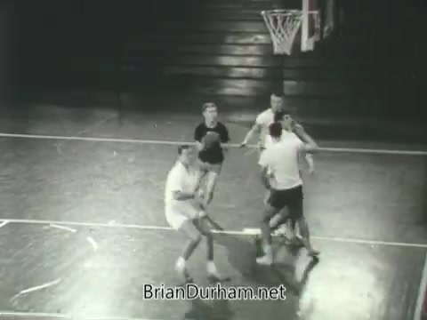 The still shows a basketball game in progress, featuring five male players on a court. The scene conveys a lively athletic environment, likely promoting physical fitness and teamwork. The players appear to be engaged in competitive play, with a focus on action and camaraderie. The image reflects the era's emphasis on youth and sportsmanship, possibly in connection with the ROTC program's values.