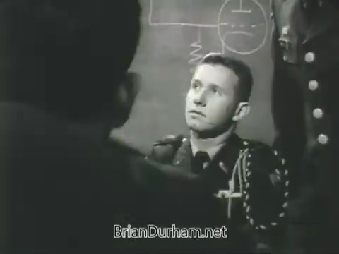 The still features a young soldier in uniform seated before a chalkboard, which has technical diagrams and equations. He appears attentive, possibly engaged in a lecture or discussion about military training. The image conveys an educational atmosphere typical of a recruitment or training setting for the US Army ROTC in the late 1960s.