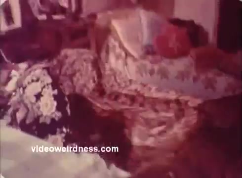 The still from the 'Won Ton Ton' movie trailer features a cluttered living area, showcasing a mix of floral-patterned fabrics and soft furnishings. The scene conveys a nostalgic, possibly comedic atmosphere indicative of the film's style. The lighting appears warm and inviting, contributing to the vintage feel of the 16mm print.