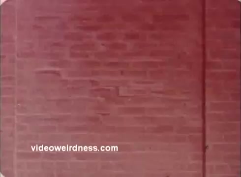 The still features a close-up of a textured brick wall, rendered in muted reddish tones. The image appears to be slightly faded, characteristic of a 16mm print. There are no identifiable characters or dialogue, focusing instead on the wall's surface and color. The presence of a watermark suggests it is part of a collection related to the film.