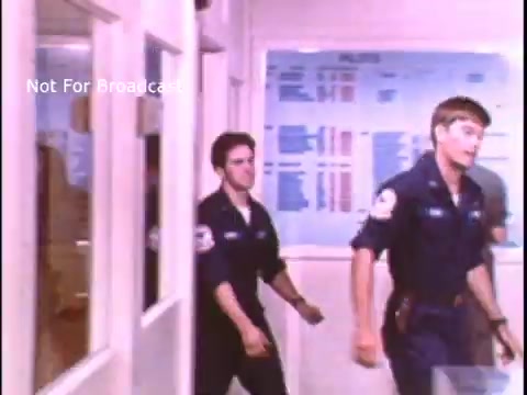 The still shows two young men in US Coast Guard uniforms walking through a corridor. The setting appears institutional, with a bulletin board or charts visible in the background. The overall tone suggests a focus on teamwork and duty typical of a public service announcement from the 1970s.