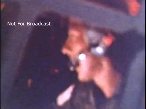 The still captures a close-up of a man, likely a member of the US Coast Guard, wearing a headset and microphone, indicating a focus on communication. The scene conveys a sense of urgency and professionalism, typical of public service announcements from the 1970s. The background appears blurred, emphasizing the individual and their role. The label 'Not For Broadcast' suggests this is a behind-the-scenes or raw shot rather than a polished final product.