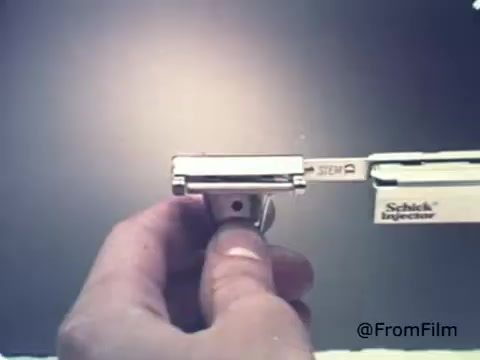 The still from the 'Schick Injector Razor Blades' advertisement showcases a hand holding a Schick Injector razor prominently. The focus is on the razor's blade mechanism, emphasizing its design and functionality. The background is minimalistic, likely to highlight the product. This promotional material reflects the 1970s aesthetic, aiming to convey efficiency and innovation in shaving technology.