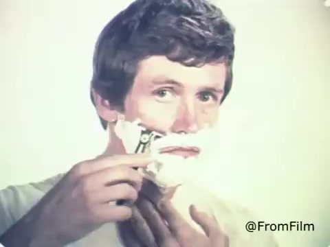 The still depicts a man applying shaving cream to his face and using a Schick Injector Razor Blade. Characterized by a clean-cut and casual look, the scene likely promotes the ease and efficiency of the razor in a relatable, everyday setting. The visuals reflect the advertising style of the 1970s, emphasizing grooming and personal care for men. The overall tone suggests familiarity and trust in the product.