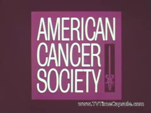 The still is from a public service announcement (PSA) by the American Cancer Society featuring astronaut Walter Schirra. The visual displays the organization's logo prominently, which consists of bold text in white reading 'AMERICAN CANCER SOCIETY' against a purple background. The logo includes graphical elements that suggest health and vigilance, supporting the message of the PSA. In the voiceover, Schirra emphasizes the importance of regular checkups and vigilance for warning signs, using a metaphor of the extensive checklist astronauts adhere to before a launch. This analogy highlights the significance of proactive health measures, paralleling space exploration's meticulous safety protocols.