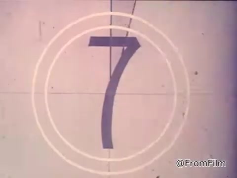 The still features a vintage 16mm countdown with the number '7' prominently displayed within concentric circles, typical of film reels from the 1970s. The context suggests a nostalgic advertisement for Nestlé semi-sweet chocolate chips, highlighting their role in making the classic Toll House cookies. The voiceover emphasizes the appeal of fresh, home-baked cookies and directs viewers to the recipe on the packaging.