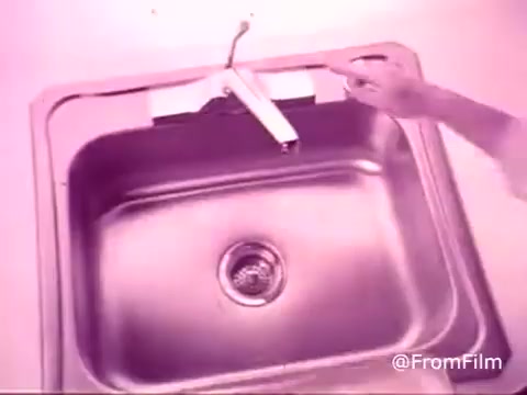 The still from the 'DuPont Lucite Wall Paint commercial' features a close-up view of a kitchen sink. The scene likely emphasizes the cleanliness and vibrant finish of Lucite paint, showcasing a person's hand pointing toward the faucet. The overall aesthetic has a vintage feel, with muted tones typical of 1970s commercials, highlighting the product's appeal for home improvement.   For more retro content, subscribe, like, or follow us on Twitter @FromFilm.