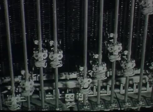 The still from 'Bell System Film - Drop Wire Runs Part 1 (a)' depicts a close-up view of a mechanical circuit switchboard commonly used in Central Offices. It shows a series of metal rods and connectors, indicative of the technology utilized to manage telephone connections in the late 1940s to early 1950s. The intricate arrangement highlights the complexity of telephone infrastructure during that period, as it functions to route calls from the telephone poles to customer lines.