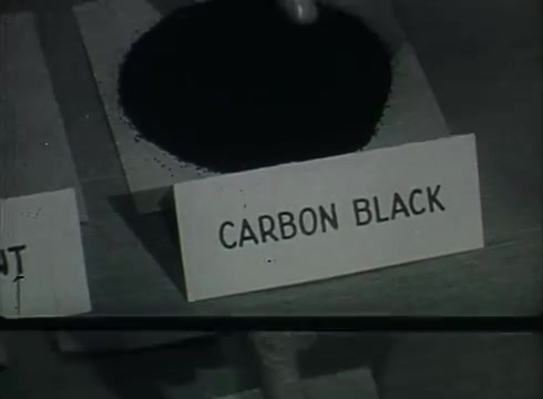 The still features a close-up of a black powder labeled 'CARBON BLACK.' It appears to be displayed on a table, likely as part of a demonstration or educational segment within the Bell System film. This film, created in the late 1940s or early 1950s, is focused on the processes involved in telephone wire installation, possibly highlighting materials used in telephone infrastructure.